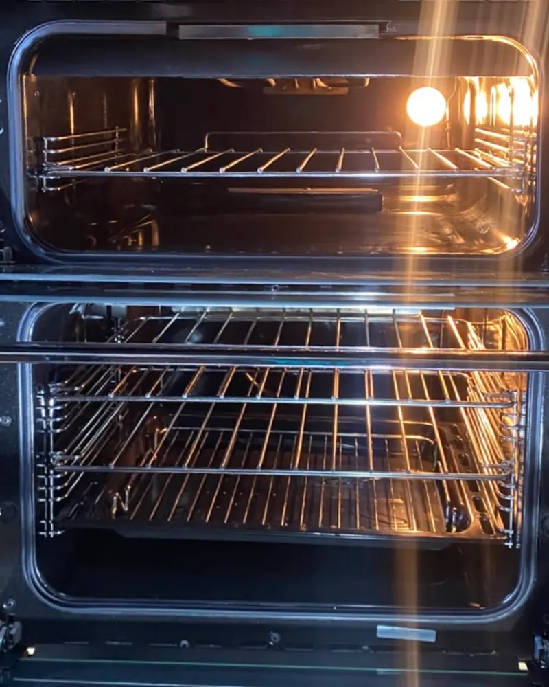 The same double oven after cleaning, both cavities lit, with clean racks, shelf runners and enamel